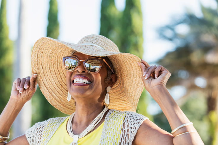 A woman wearing sunglasses and a hat grins while looking into the distance.