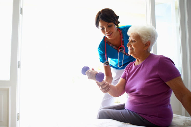 A woman uses a hand weight with the supervision of a care professional.