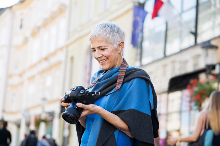 A woman stands outside a building with her camera.