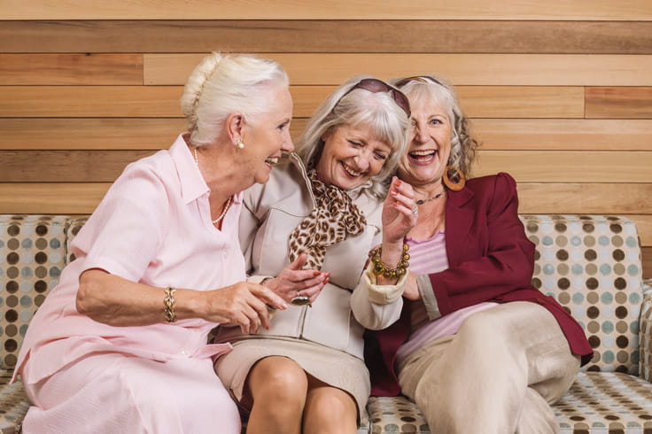 Three women laugh together on a sofa.