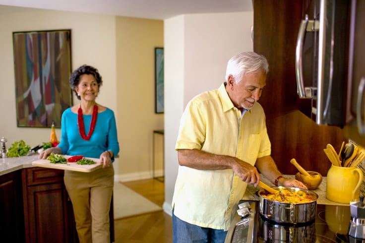 A man cooks a meal while a woman walks toward him with ingredients.
