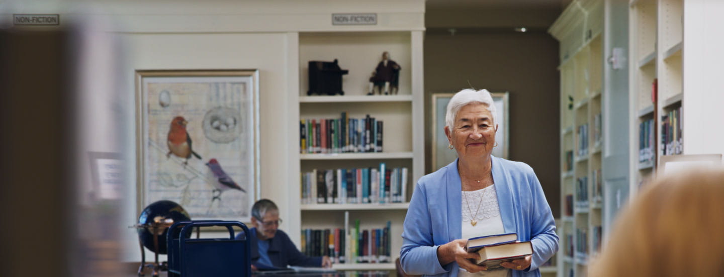 A woman walks toward a library circulation desk with books in hand.