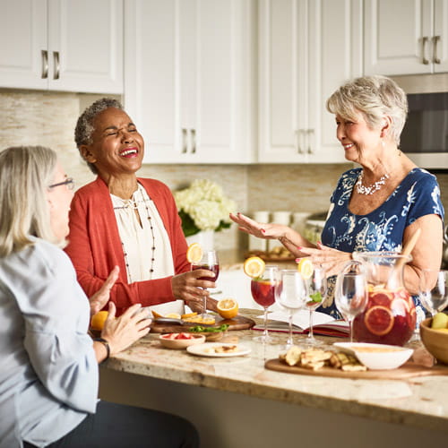 Three women laugh while they drink sangria in an apartment.