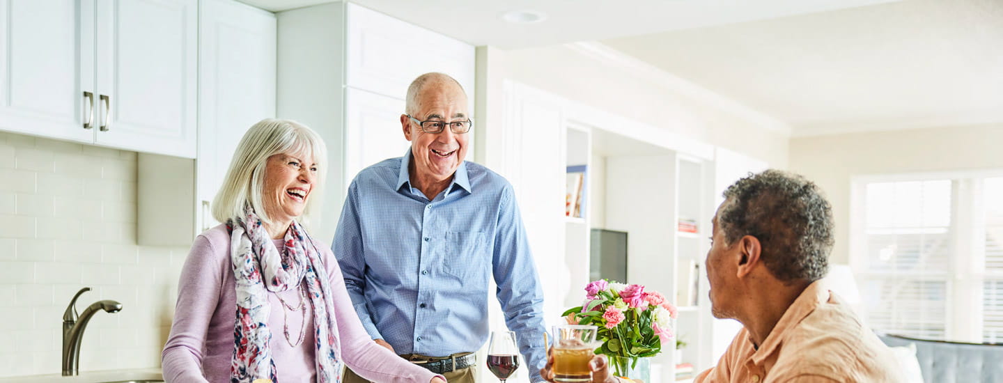 A couple serves drinks to a friend in the kitchen.