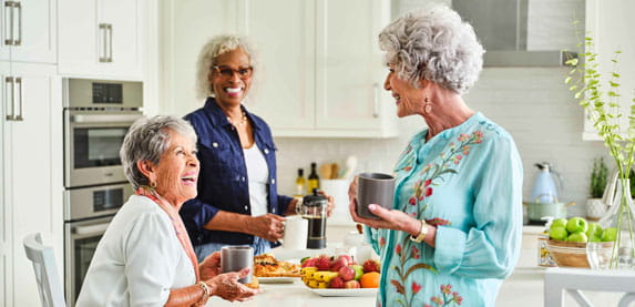Three women socialize together in the kitchen.