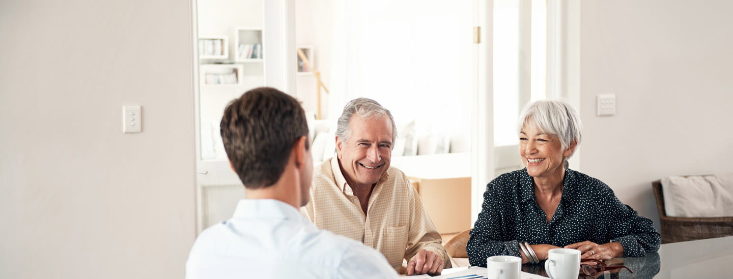 Two older people smile and talk with a man who is facing away from the camera.