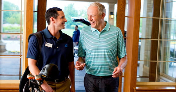 An employee carries golf clubs while talking to a resident.