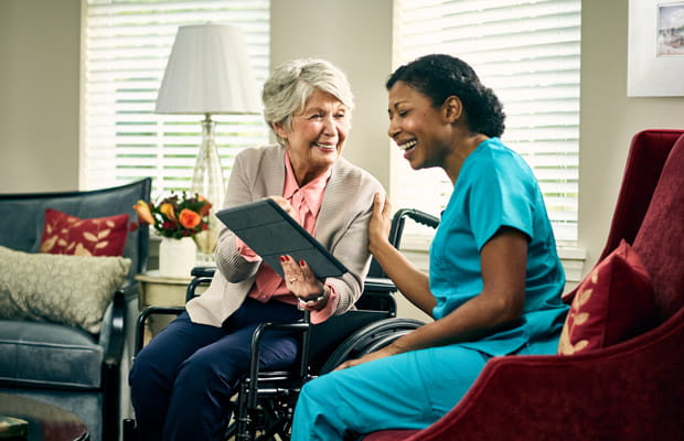 A woman in a wheelchair shows a tablet to a care worker.