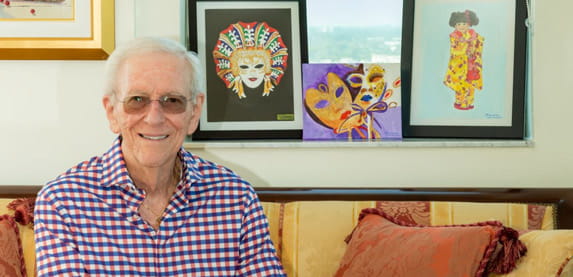 Vi at Aventura resident Hank Solomon sits with his watercolor paintings in the background.
