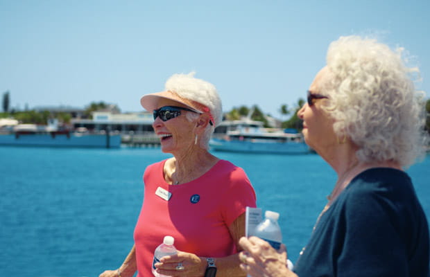 Two women laugh while standing next to a body of water.
